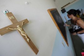 A teacher writes on a chalkboard with a crucifix in the foreground